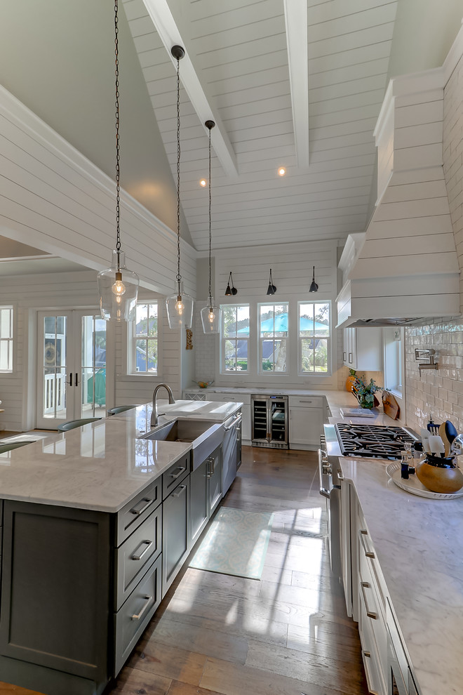Example of a large trendy u-shaped light wood floor and brown floor open concept kitchen design in Charleston with white cabinets, marble countertops, white backsplash, glass tile backsplash, stainless steel appliances and an island