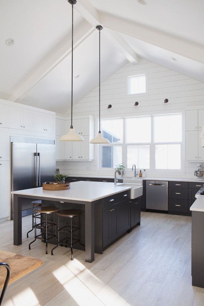 Foto de cocina de estilo de casa de campo de tamaño medio con armarios estilo shaker, una isla, salpicadero blanco, electrodomésticos de acero inoxidable y suelo de madera clara