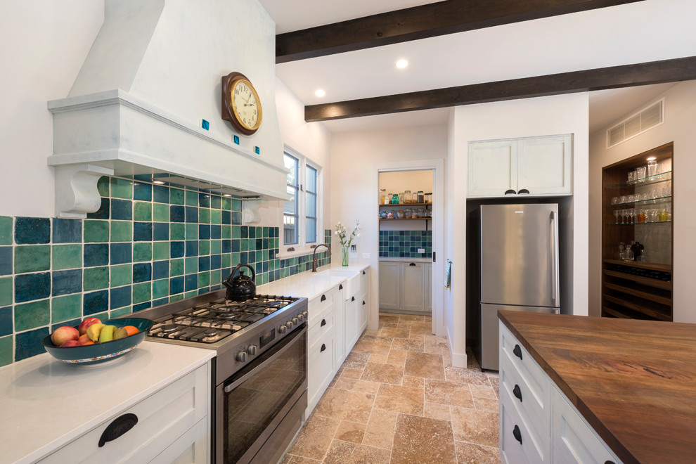 Inspiration for a large mediterranean galley travertine floor kitchen pantry remodel in Melbourne with a farmhouse sink, shaker cabinets, white cabinets, multicolored backsplash, stainless steel appliances, an island, terra-cotta backsplash and quartz countertops