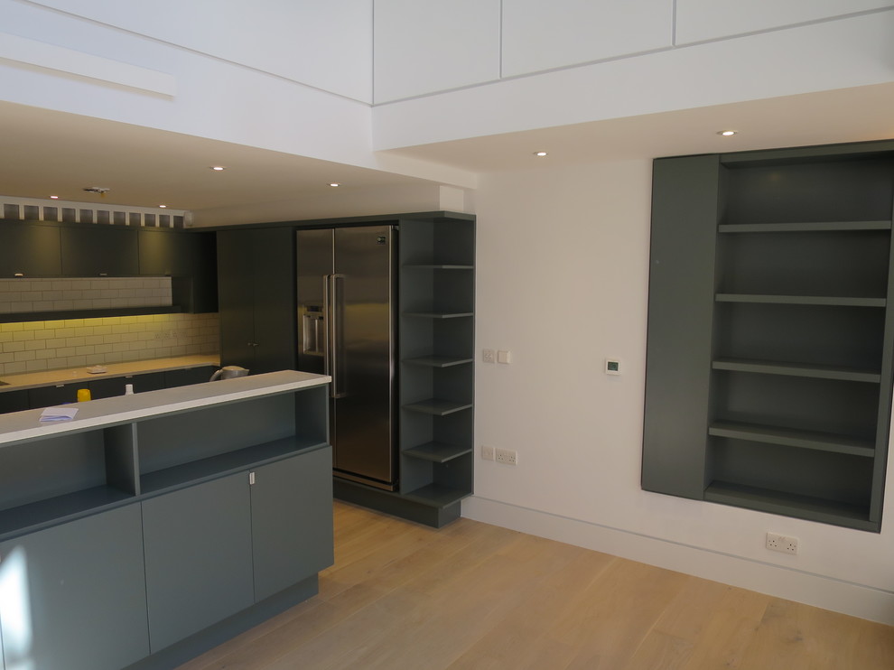 Design ideas for a large contemporary l-shaped kitchen/diner in London with an integrated sink, flat-panel cabinets, turquoise cabinets, composite countertops, white splashback, metro tiled splashback, stainless steel appliances, light hardwood flooring, an island and beige floors.