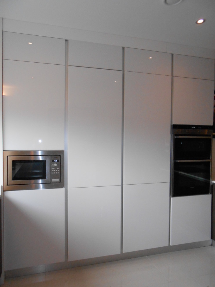 Large single-wall open plan kitchen in London with flat-panel cabinets, white cabinets, stainless steel appliances, ceramic flooring, no island and beige floors.