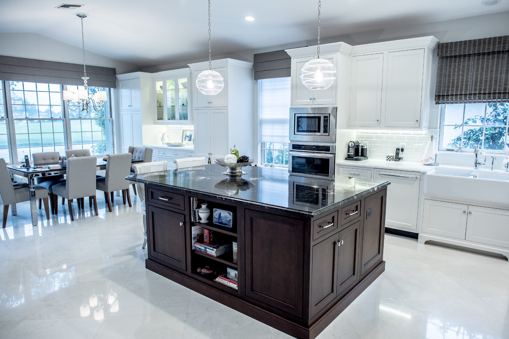Example of a mid-sized trendy l-shaped porcelain tile open concept kitchen design in Miami with a farmhouse sink, shaker cabinets, white cabinets, marble countertops, white backsplash, subway tile backsplash, stainless steel appliances and an island