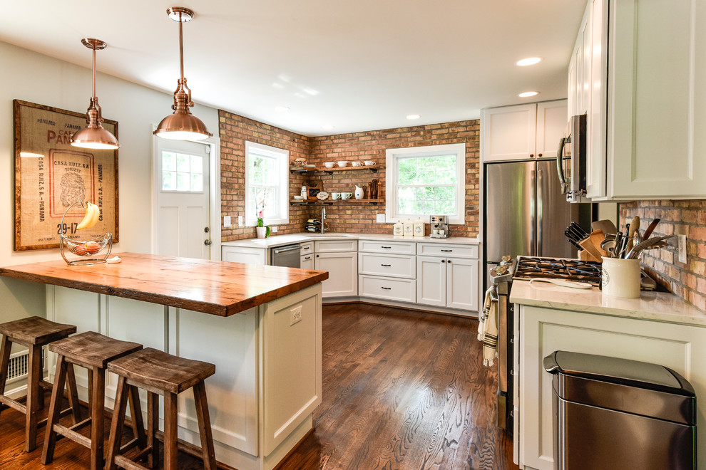 Example of a mid-sized country u-shaped dark wood floor and brown floor enclosed kitchen design in DC Metro with an undermount sink, shaker cabinets, white cabinets, wood countertops, red backsplash, brick backsplash, stainless steel appliances and a peninsula