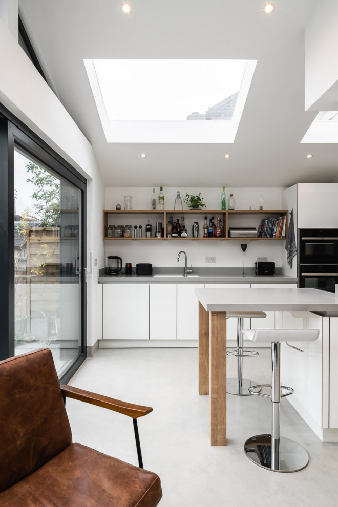 Offene Moderne Küche mit flächenbündigen Schrankfronten, weißen Schränken, schwarzen Elektrogeräten, Kücheninsel, grauem Boden, grauer Arbeitsplatte und gewölbter Decke in Glasgow