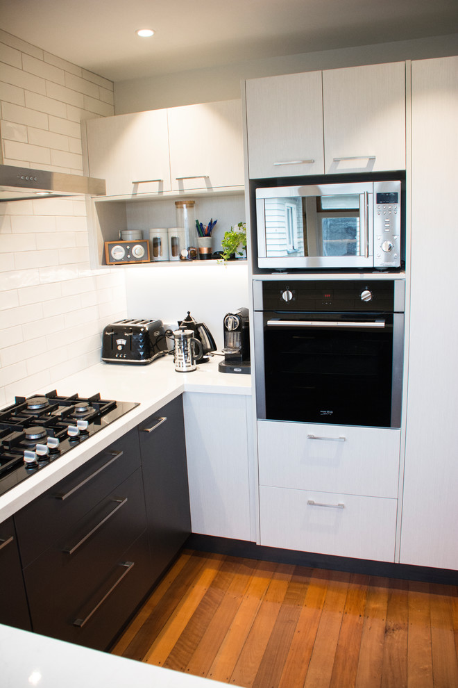 Inredning av ett modernt mellanstort kök, med en dubbel diskho, svarta skåp, laminatbänkskiva, vitt stänkskydd, stänkskydd i tunnelbanekakel, rostfria vitvaror och mellanmörkt trägolv