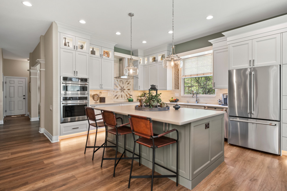 Inspiration for a large transitional l-shaped medium tone wood floor and brown floor open concept kitchen remodel in Other with an undermount sink, recessed-panel cabinets, white cabinets, beige backsplash, stainless steel appliances, an island, beige countertops, quartz countertops and subway tile backsplash