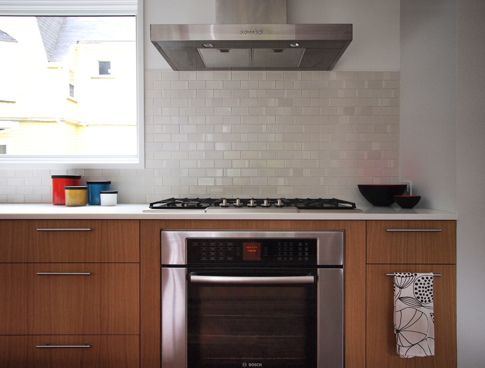 ニューヨークにあるモダンスタイルのおしゃれなキッチン (一体型シンク、フラットパネル扉のキャビネット、中間色木目調キャビネット、人工大理石カウンター、白いキッチンパネル、セラミックタイルのキッチンパネル、シルバーの調理設備、濃色無垢フローリング) の写真