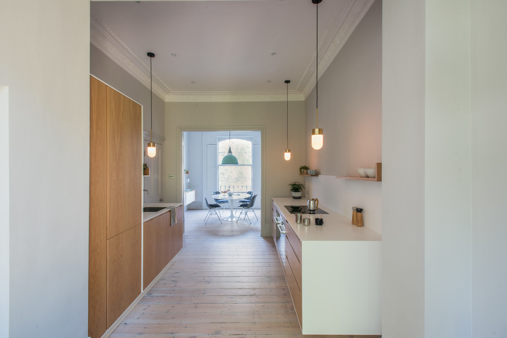 This is an example of a medium sized modern galley kitchen/diner in London with a submerged sink, flat-panel cabinets, light wood cabinets, quartz worktops, integrated appliances, light hardwood flooring and brown floors.
