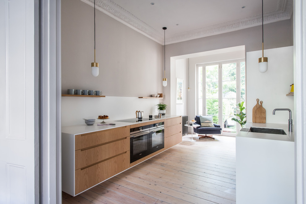 Inspiration for a medium sized modern galley kitchen/diner in London with white splashback, light hardwood flooring, a submerged sink, flat-panel cabinets, light wood cabinets, quartz worktops, integrated appliances and brown floors.