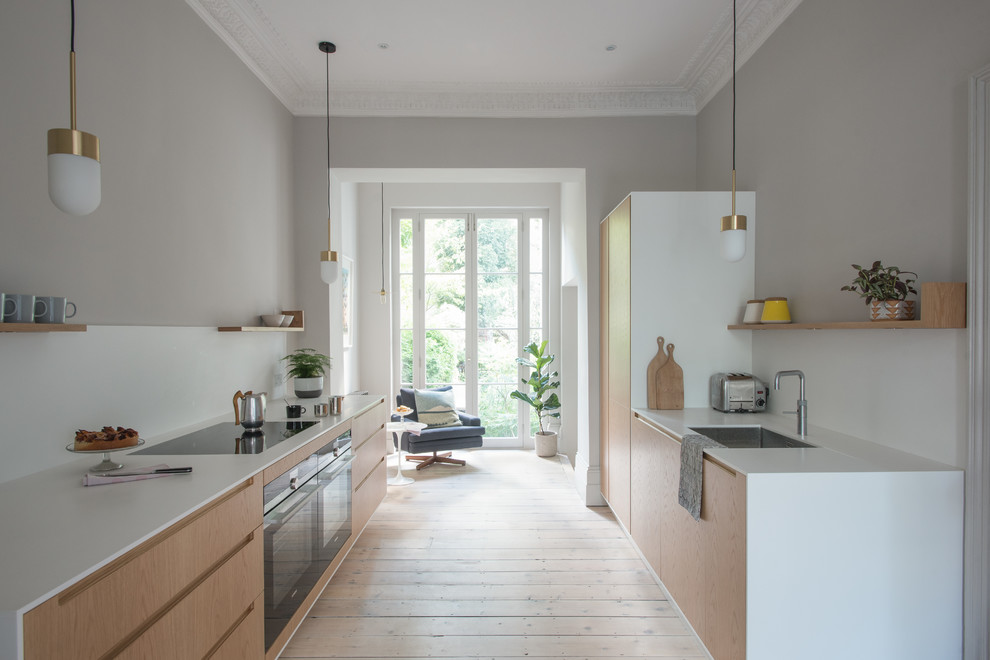 Inspiration for a medium sized modern galley kitchen/diner in London with white splashback, light hardwood flooring, a submerged sink, flat-panel cabinets, light wood cabinets, quartz worktops, integrated appliances and brown floors.