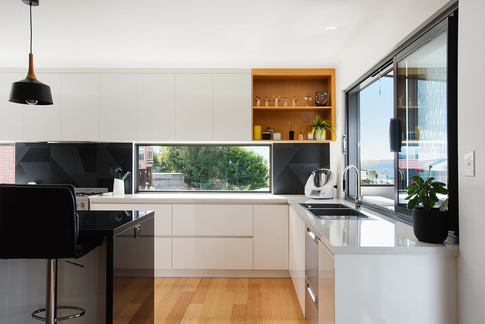 Immagine di una cucina minimalista di medie dimensioni con lavello da incasso, ante bianche, top in laminato, paraspruzzi a finestra, elettrodomestici in acciaio inossidabile e pavimento in laminato