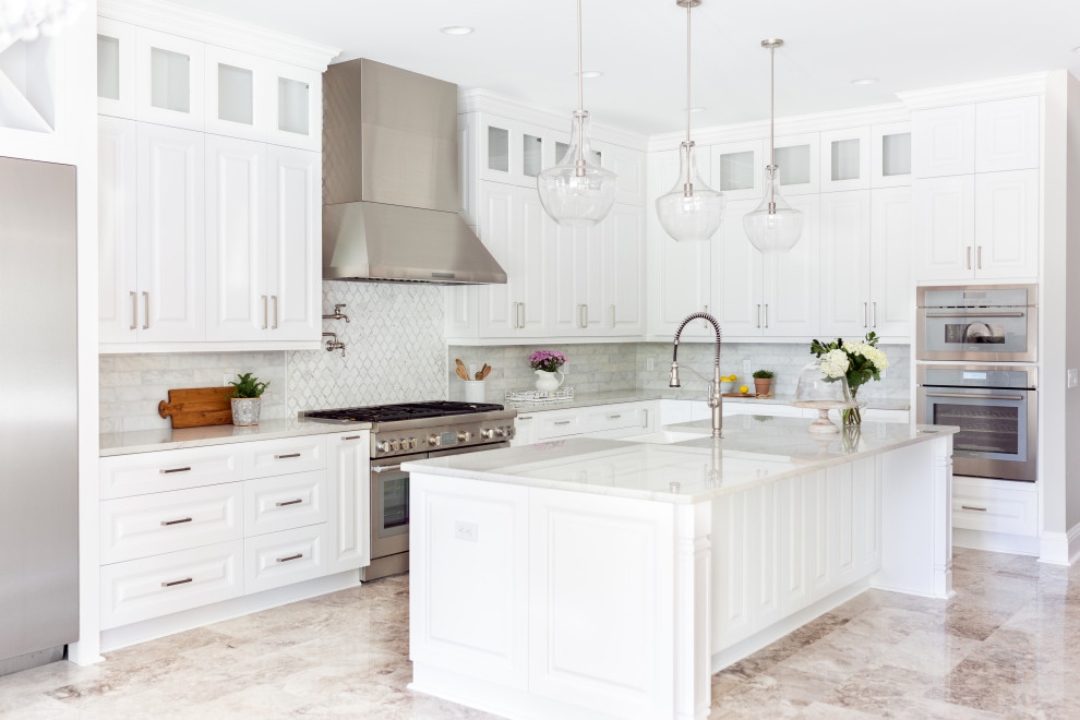 This is an example of a traditional l-shaped kitchen in Jacksonville with a belfast sink, white cabinets, quartz worktops, marble splashback, stainless steel appliances, marble flooring, an island, white worktops, raised-panel cabinets, grey splashback and beige floors.