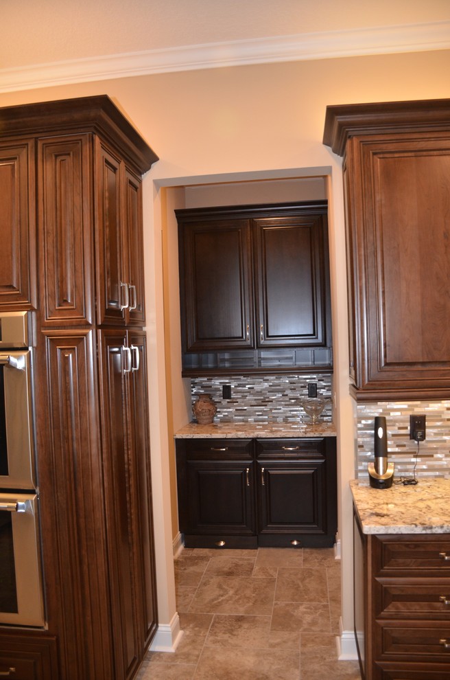 Bild på ett avskilt, stort eklektiskt u-kök, med en undermonterad diskho, luckor med upphöjd panel, skåp i mörkt trä, granitbänkskiva, stänkskydd med metallisk yta, stänkskydd i stickkakel, rostfria vitvaror, klinkergolv i porslin och flera köksöar