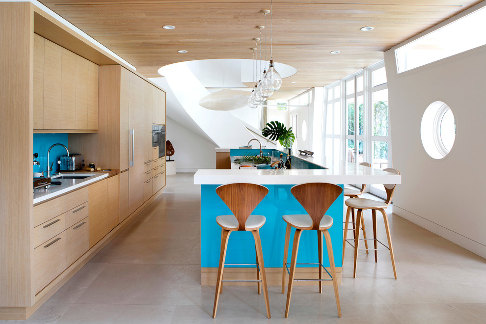 Immagine di una grande cucina design con ante lisce, ante in legno chiaro, paraspruzzi blu, lavello sottopiano, paraspruzzi con lastra di vetro, elettrodomestici in acciaio inossidabile, pavimento beige e pavimento in laminato