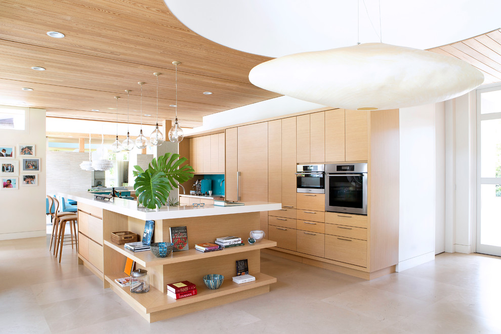 Photo of a large contemporary single-wall open plan kitchen in Miami with a submerged sink, flat-panel cabinets, light wood cabinets, blue splashback, glass sheet splashback, stainless steel appliances, an island, beige floors and limestone flooring.