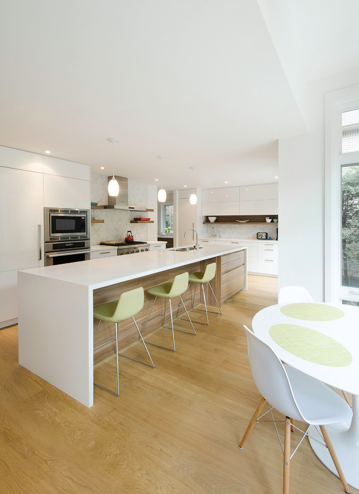 Bild på ett funkis kök, med släta luckor, vita skåp, vitt stänkskydd, rostfria vitvaror, mellanmörkt trägolv och en köksö
