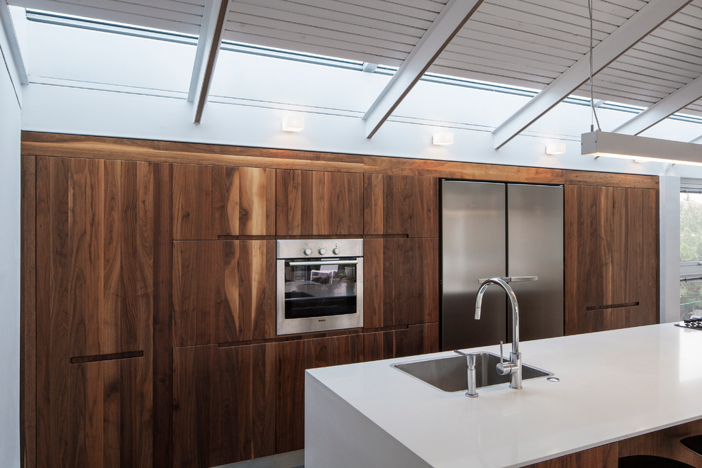 Cette image montre une cuisine minimaliste en bois foncé avec un évier posé, un placard à porte plane et un électroménager en acier inoxydable.