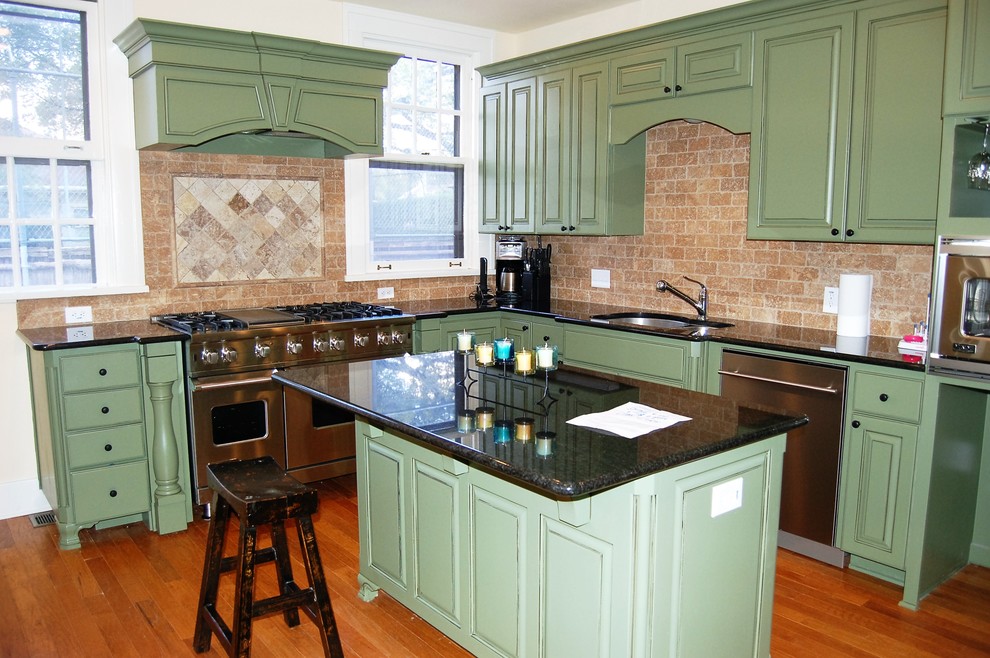 Photo of a medium sized classic l-shaped kitchen/diner in Austin with a double-bowl sink, raised-panel cabinets, green cabinets, granite worktops, red splashback, stone tiled splashback, stainless steel appliances, medium hardwood flooring and an island.