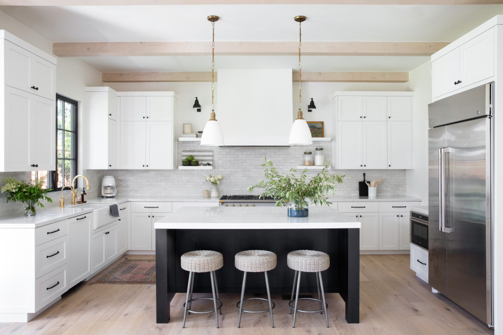 Kitchen - coastal u-shaped light wood floor, beige floor and exposed beam kitchen idea in San Francisco with a farmhouse sink, shaker cabinets, white cabinets, white backsplash, stainless steel appliances, an island and white countertops