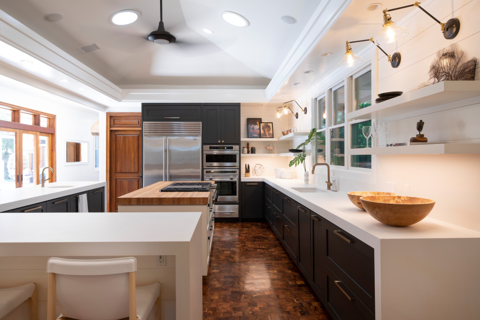 Example of an island style u-shaped dark wood floor, brown floor and vaulted ceiling kitchen design in Hawaii with an undermount sink, shaker cabinets, black cabinets, stainless steel appliances, two islands and white countertops