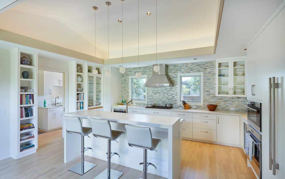 Example of a trendy u-shaped medium tone wood floor and brown floor kitchen design in Hawaii with flat-panel cabinets, white cabinets, multicolored backsplash, matchstick tile backsplash, paneled appliances, an island and white countertops