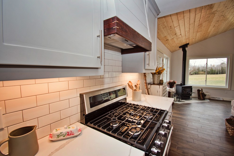 他の地域にある高級な広いカントリー風のおしゃれなキッチン (エプロンフロントシンク、落し込みパネル扉のキャビネット、白いキャビネット、大理石カウンター、白いキッチンパネル、サブウェイタイルのキッチンパネル、シルバーの調理設備、無垢フローリング、茶色い床、白いキッチンカウンター) の写真