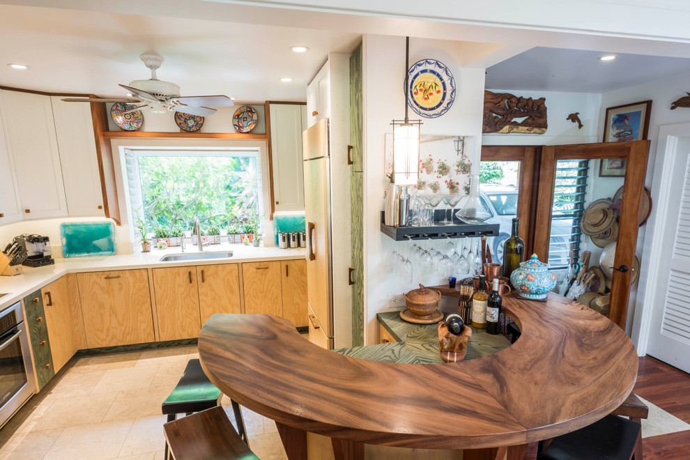 Example of a mid-sized island style u-shaped travertine floor and beige floor enclosed kitchen design in Hawaii with an undermount sink, beaded inset cabinets, light wood cabinets, wood countertops, paneled appliances and a peninsula