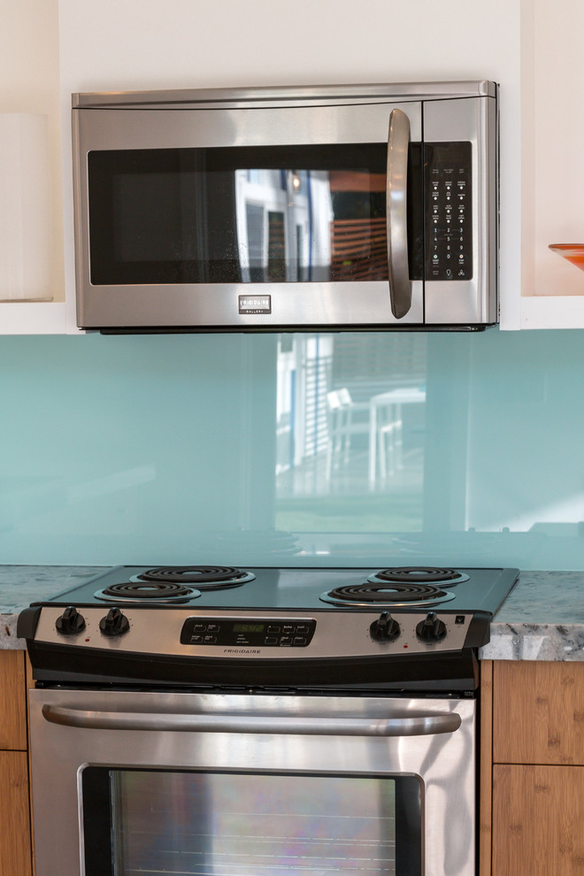 Bild på ett mellanstort maritimt kök, med en undermonterad diskho, släta luckor, skåp i ljust trä, granitbänkskiva, blått stänkskydd, glaspanel som stänkskydd, rostfria vitvaror och betonggolv