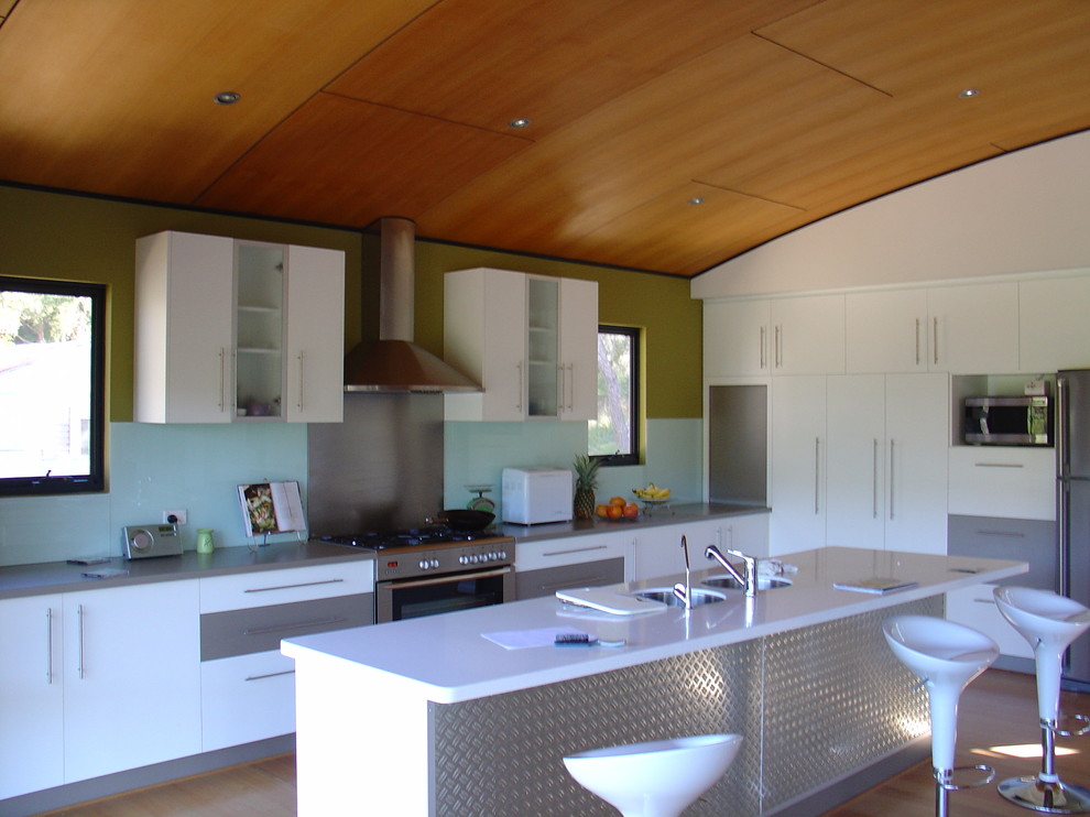 Example of a mid-sized minimalist l-shaped light wood floor eat-in kitchen design in Perth with an undermount sink, white cabinets, multicolored backsplash, glass sheet backsplash, stainless steel appliances, an island, flat-panel cabinets, solid surface countertops and white countertops