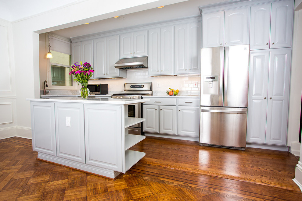 Klassisk inredning av ett litet kök, med en dubbel diskho, luckor med upphöjd panel, grå skåp, marmorbänkskiva, vitt stänkskydd, stänkskydd i keramik, rostfria vitvaror, mellanmörkt trägolv och en köksö