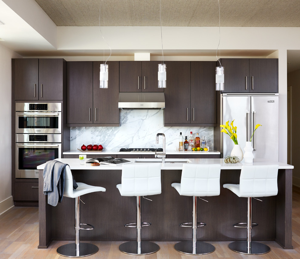 Foto de cocina contemporánea de tamaño medio abierta con fregadero bajoencimera, armarios con paneles lisos, puertas de armario de madera en tonos medios, encimera de acrílico, salpicadero blanco, salpicadero de losas de piedra, electrodomésticos de acero inoxidable, suelo de madera en tonos medios, una isla y suelo marrón