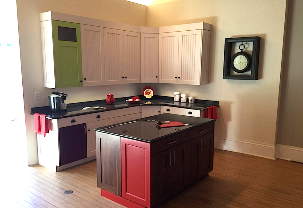 Example of a small eclectic l-shaped medium tone wood floor enclosed kitchen design in Milwaukee with louvered cabinets, white cabinets, solid surface countertops, black backsplash, stone slab backsplash and an island