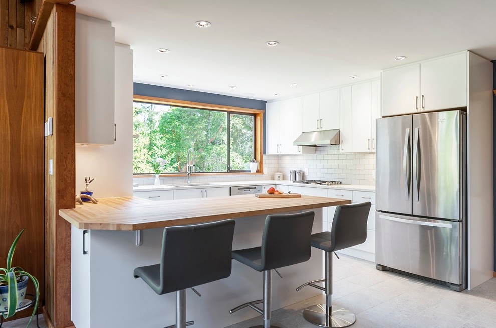 Medium sized scandi u-shaped open plan kitchen in Other with a submerged sink, flat-panel cabinets, white cabinets, engineered stone countertops, white splashback, metro tiled splashback, stainless steel appliances, porcelain flooring, a breakfast bar and white worktops.