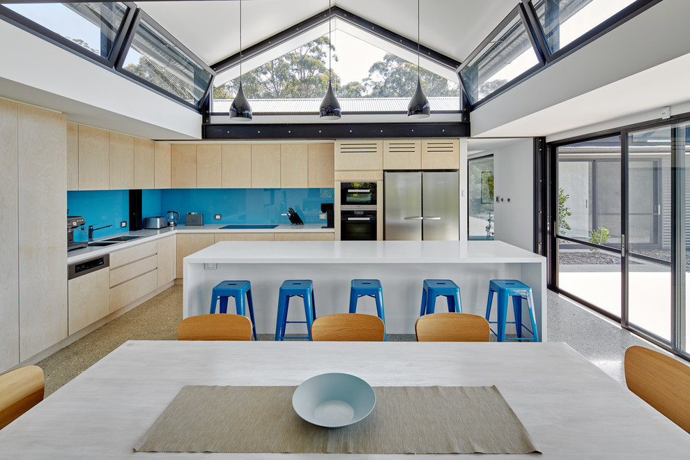 Esempio di una grande cucina minimal con lavello a doppia vasca, ante in legno chiaro, paraspruzzi blu, paraspruzzi con lastra di vetro, elettrodomestici in acciaio inossidabile, pavimento in cemento, ante lisce e top in quarzo composito