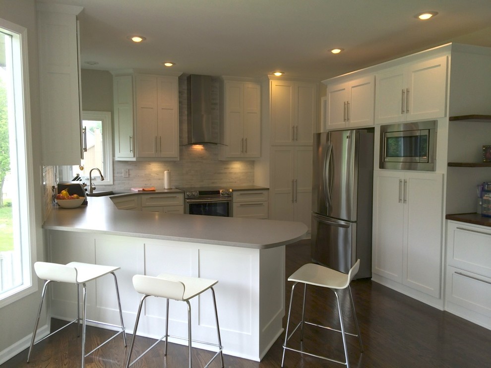 Photo of a medium sized classic u-shaped kitchen/diner in Kansas City with a submerged sink, shaker cabinets, white cabinets, engineered stone countertops, white splashback, stainless steel appliances, dark hardwood flooring and a breakfast bar.