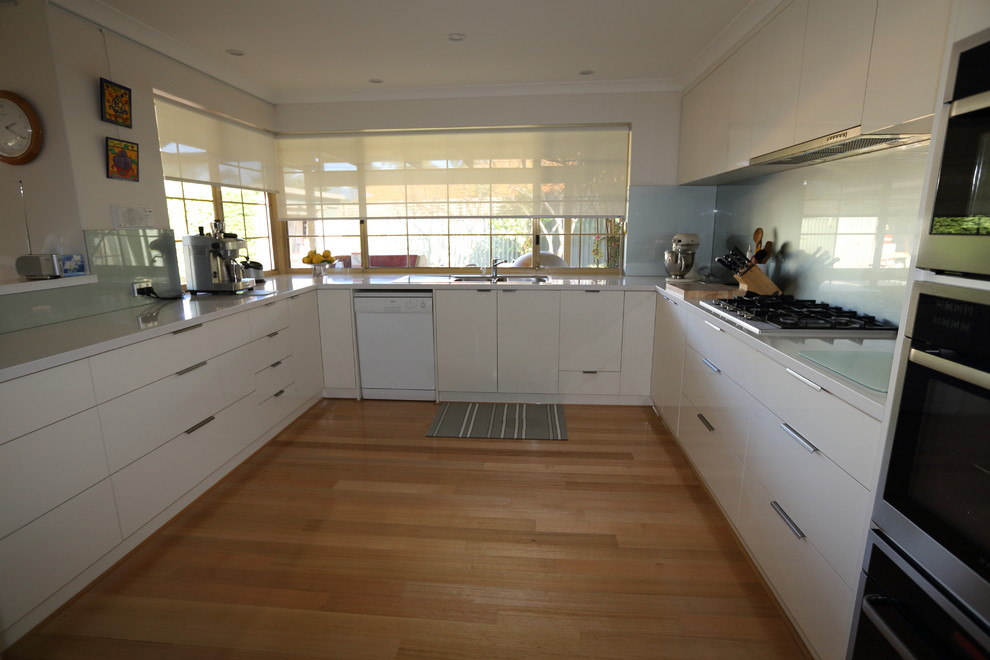 Modern inredning av ett mellanstort kök, med en dubbel diskho, släta luckor, vita skåp, bänkskiva i kvarts, grönt stänkskydd, glaspanel som stänkskydd, rostfria vitvaror, mellanmörkt trägolv och en köksö