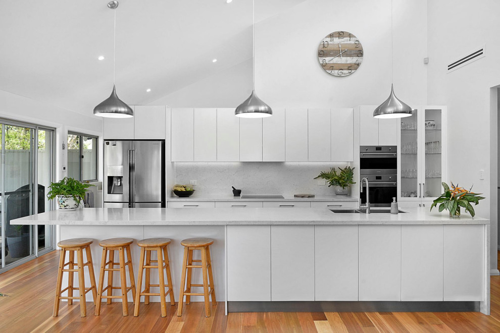 Inspiration for a contemporary galley kitchen in Adelaide with a submerged sink, flat-panel cabinets, white cabinets, grey splashback, stainless steel appliances, medium hardwood flooring, an island, brown floors, grey worktops and a vaulted ceiling.