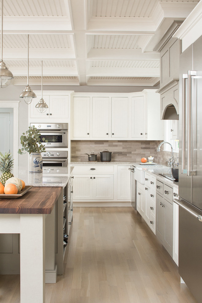 Kitchen - coastal l-shaped light wood floor and beige floor kitchen idea in Portland Maine with white cabinets, a farmhouse sink, recessed-panel cabinets, wood countertops, beige backsplash, stainless steel appliances and two islands