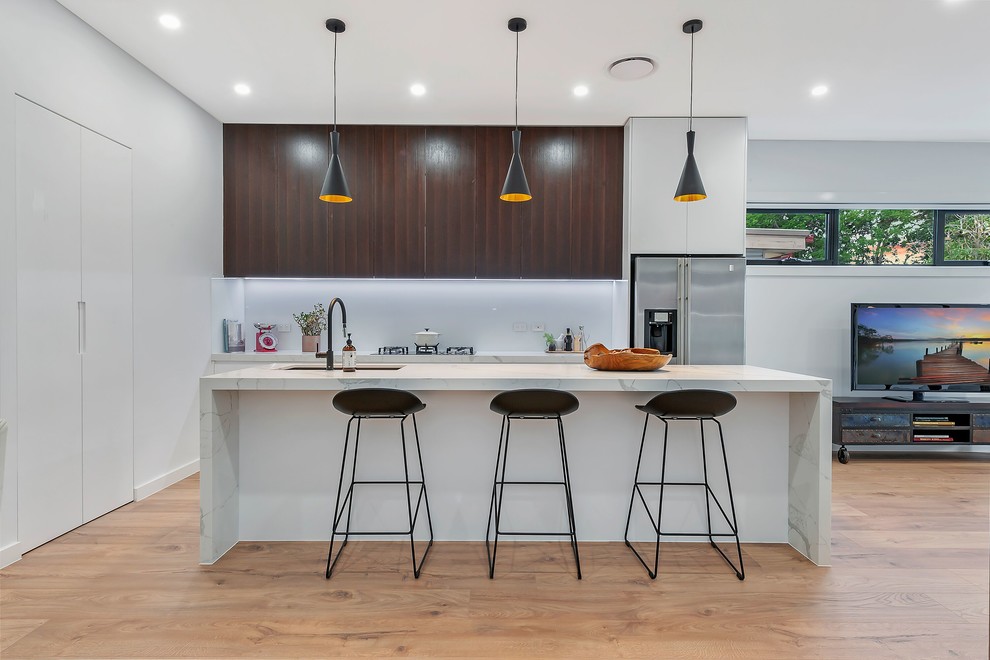 Immagine di una cucina minimal con lavello sottopiano, ante lisce, ante bianche, elettrodomestici in acciaio inossidabile, pavimento in legno massello medio, pavimento marrone e top bianco
