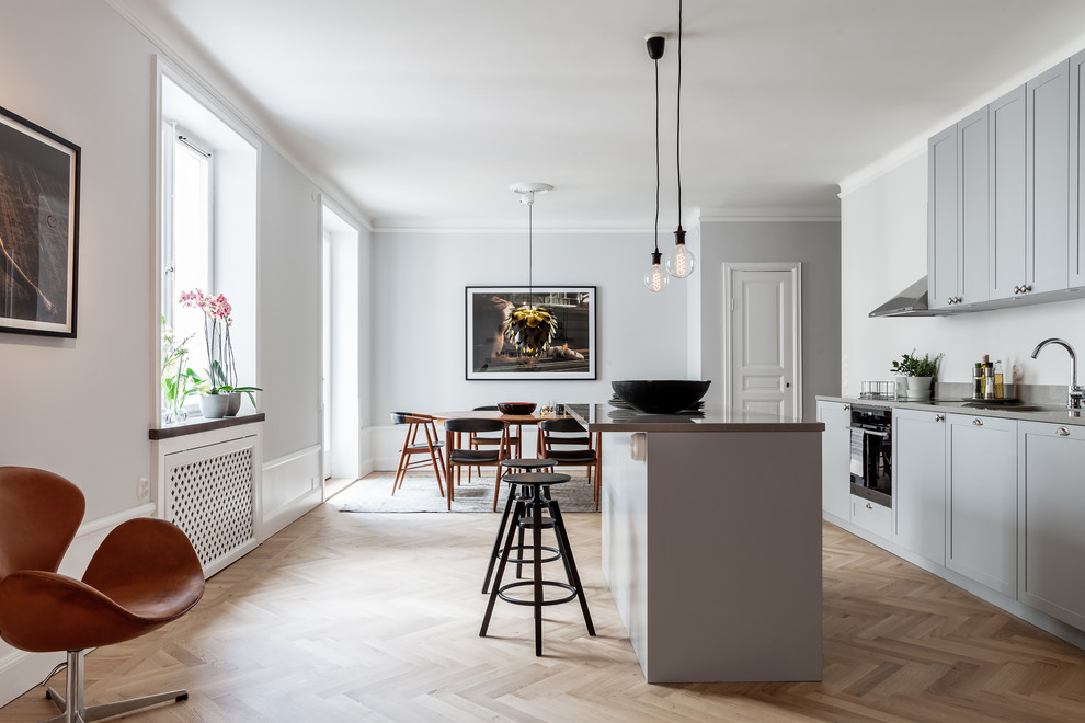Zweizeilige Skandinavische Wohnküche mit Unterbauwaschbecken, Schrankfronten mit vertiefter Füllung, grauen Schränken, Küchenrückwand in Weiß, hellem Holzboden, Kücheninsel, beigem Boden und grauer Arbeitsplatte in Sonstige