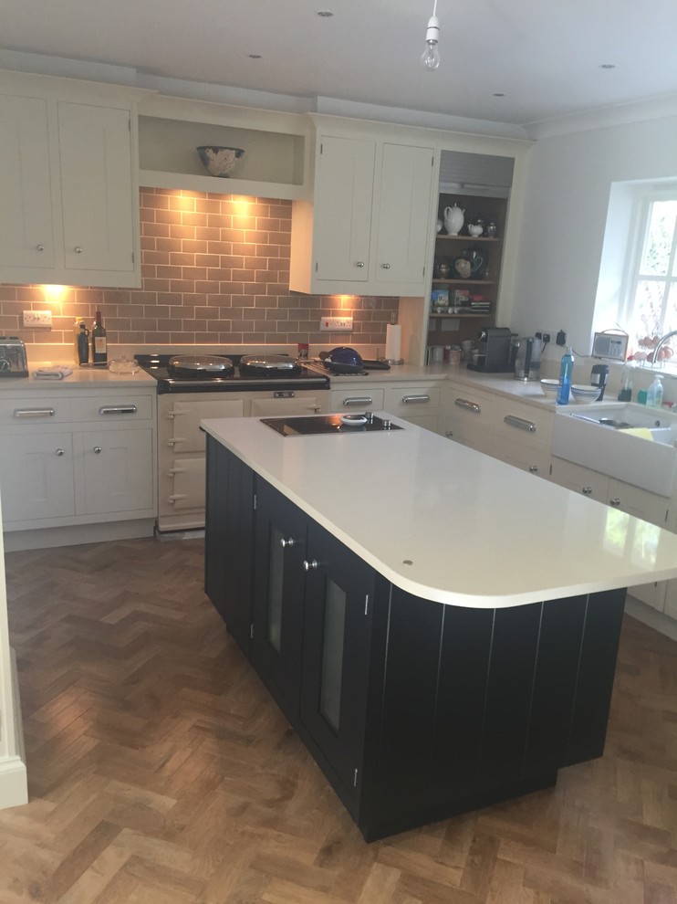 This is an example of a large country l-shaped kitchen/diner in Manchester with a belfast sink, recessed-panel cabinets, white cabinets, ceramic splashback and an island.