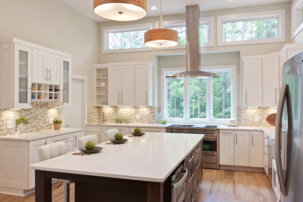 Expansive contemporary u-shaped kitchen/diner in Atlanta with a belfast sink, shaker cabinets, white cabinets, engineered stone countertops, beige splashback, glass tiled splashback, stainless steel appliances, porcelain flooring, an island, beige floors and white worktops.