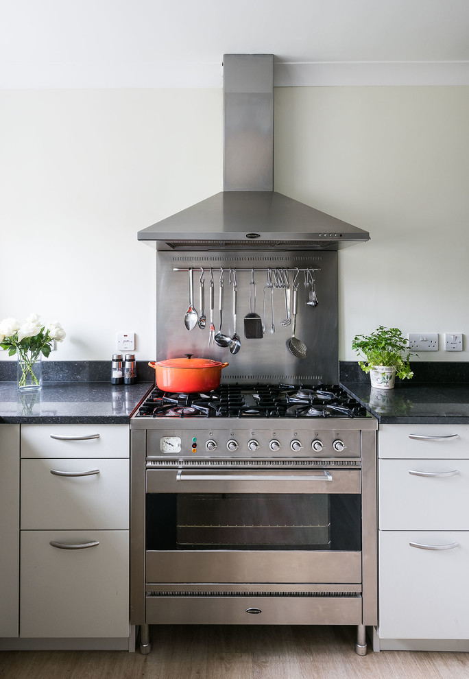 Inredning av ett modernt mellanstort svart svart kök, med en undermonterad diskho, släta luckor, grå skåp, bänkskiva i kvartsit, svart stänkskydd, rostfria vitvaror, laminatgolv och beiget golv