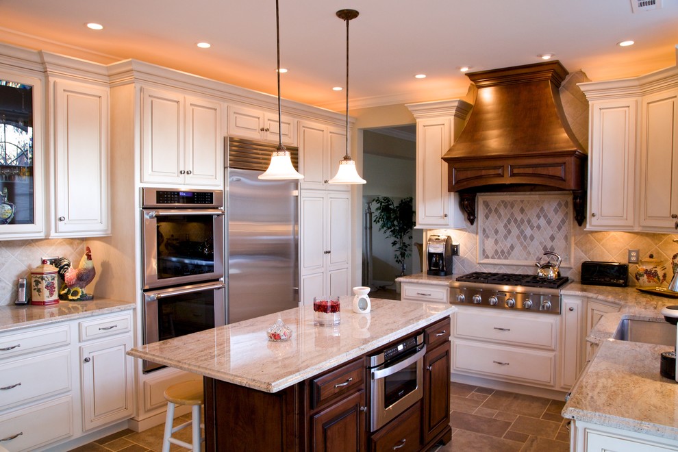 Exempel på ett stort klassiskt kök, med en undermonterad diskho, granitbänkskiva, rostfria vitvaror, luckor med upphöjd panel, vita skåp, beige stänkskydd, travertin golv och en köksö