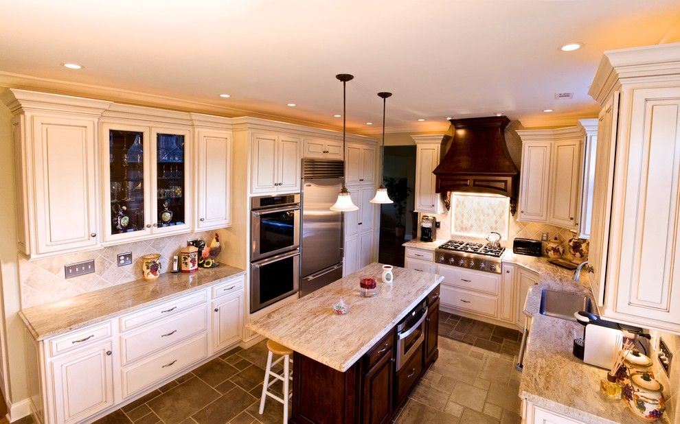 Foto på ett stort vintage kök, med en undermonterad diskho, granitbänkskiva, rostfria vitvaror, luckor med upphöjd panel, vita skåp, beige stänkskydd, travertin golv och en köksö