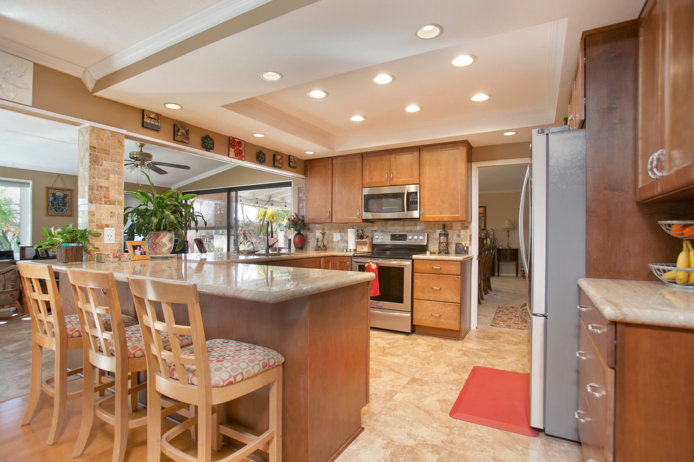 Photo of a medium sized traditional u-shaped kitchen/diner in San Diego with a single-bowl sink, recessed-panel cabinets, medium wood cabinets, granite worktops, multi-coloured splashback, travertine splashback, stainless steel appliances, porcelain flooring, a breakfast bar and multi-coloured floors.