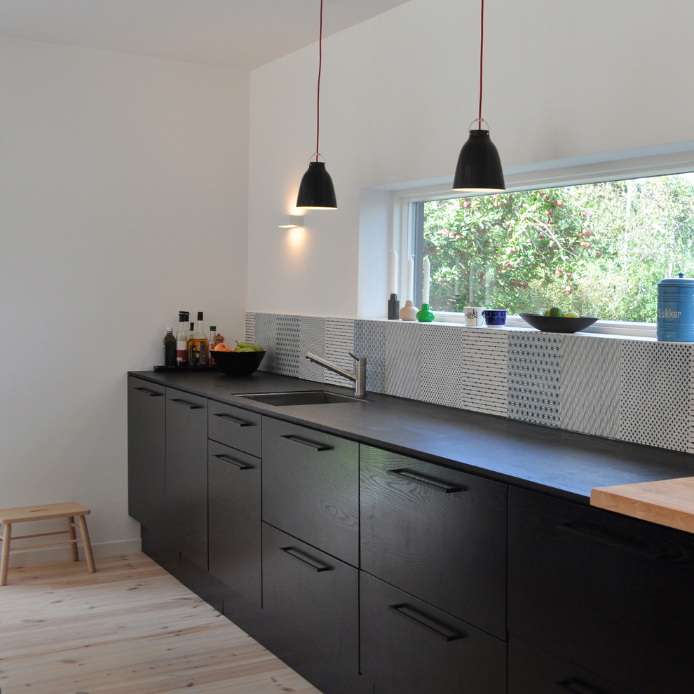 Photo of a medium sized scandinavian galley enclosed kitchen in Copenhagen with a submerged sink, flat-panel cabinets, black cabinets, multi-coloured splashback and light hardwood flooring.