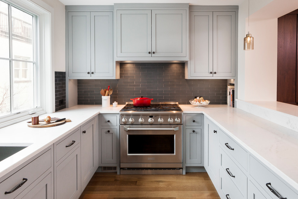 Inspiration for a large transitional u-shaped medium tone wood floor eat-in kitchen remodel in Philadelphia with an undermount sink, shaker cabinets, gray cabinets, quartz countertops, black backsplash, glass tile backsplash, stainless steel appliances and a peninsula