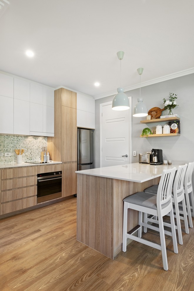 Bild på ett litet skandinaviskt vit vitt kök, med en undermonterad diskho, släta luckor, skåp i ljust trä, bänkskiva i kvarts, grönt stänkskydd, stänkskydd i marmor, rostfria vitvaror, vinylgolv, en köksö och beiget golv