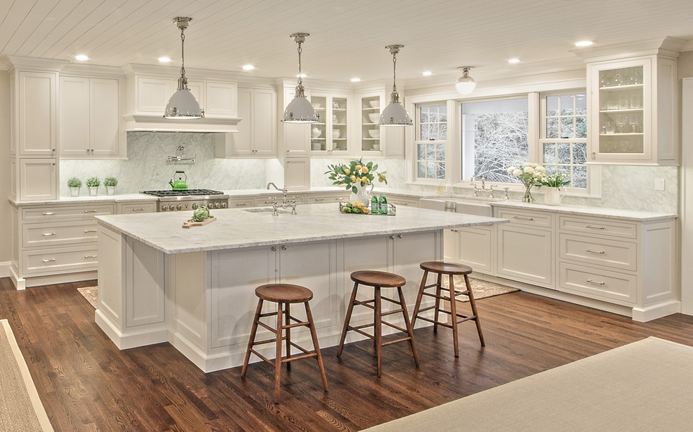 Inredning av ett klassiskt avskilt, stort vit vitt u-kök, med en rustik diskho, luckor med profilerade fronter, vita skåp, marmorbänkskiva, vitt stänkskydd, stänkskydd i marmor, integrerade vitvaror, mellanmörkt trägolv, en köksö och brunt golv